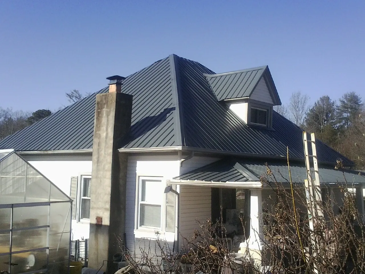 Dark blue standing seam metal roof on a white farmhouse with dormer — Slate & Tile Roof Repair by Roofing Brothers in Justice