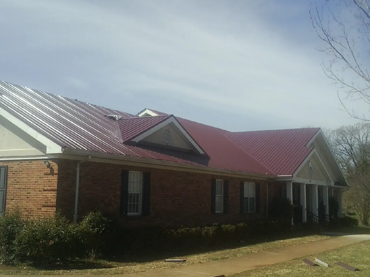 Red metal roof with gabled entries on a long brick building, from a Hail Damage Roof Repair job in Justice
