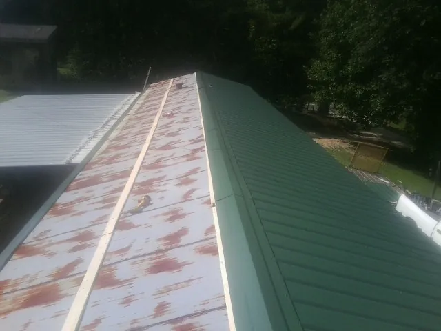 Old rusted panels beside newly installed green metal roofing — Wind Damage Roof Repair by Roofing Brothers in Justice