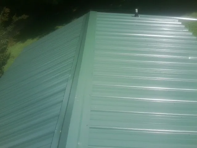 New green metal panels meeting at the ridge of a roof — Flat Roof Repair work by our crew in Justice