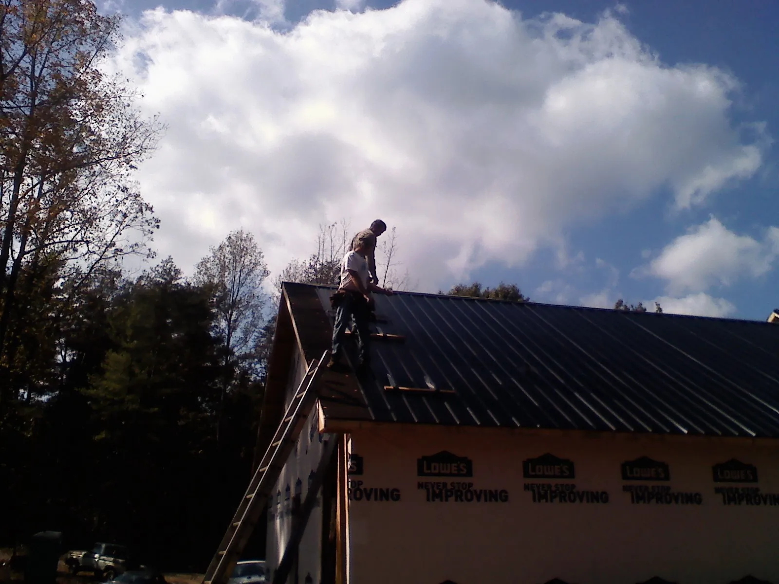 Roofer fastening dark metal panels high against a cloudy sky, from a Roof Inspection job in Justice