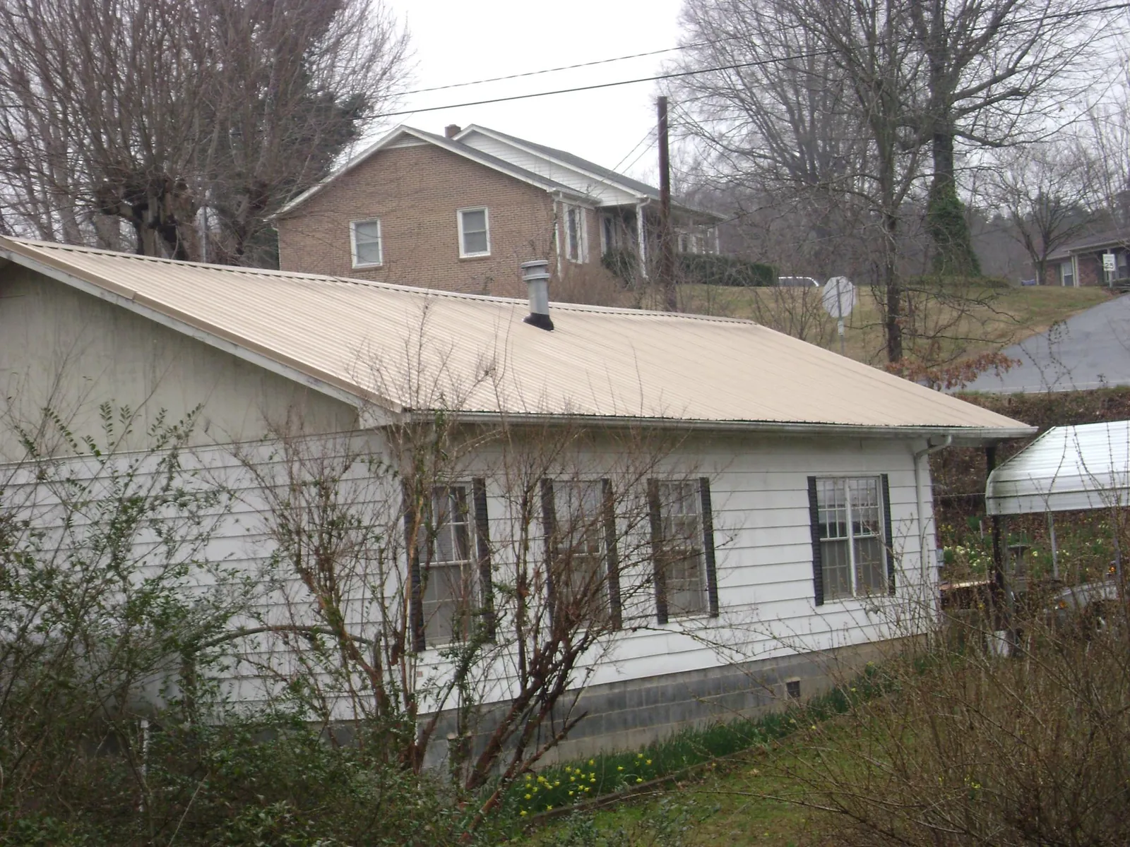 Tan metal roof on a white sided house set into a hillside — Commercial Roofing by Roofing Brothers in Justice