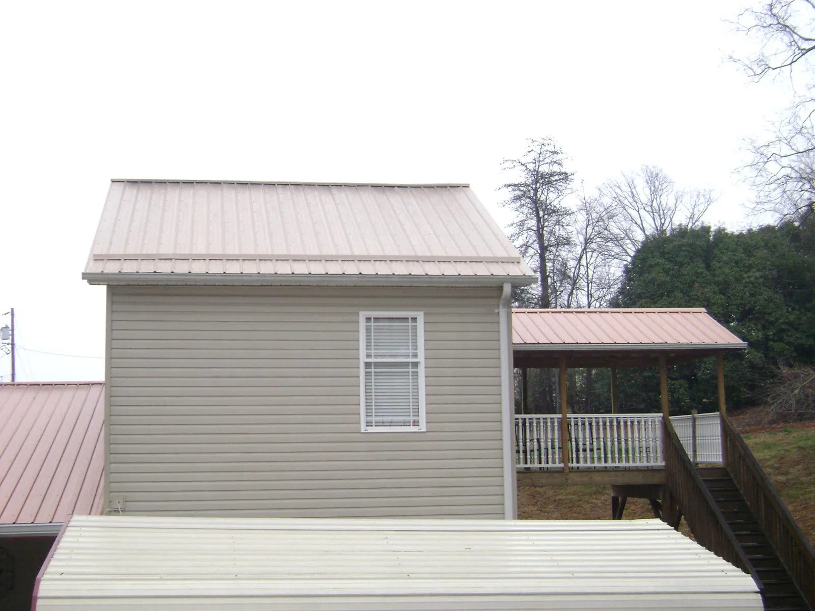 Tan metal roofs on a two story addition and attached porch, from a Roof Replacement job in Justice